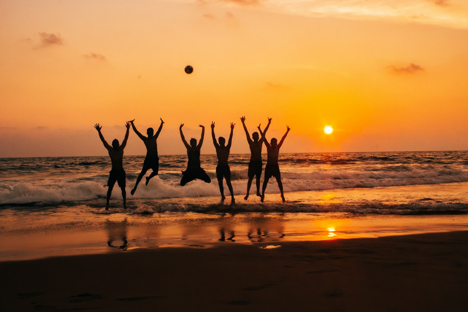 Pessoas pulando de alegria na praia ao pôr do sol