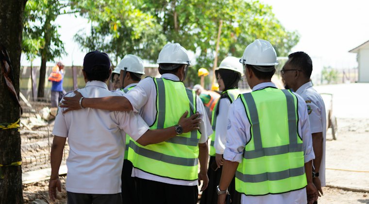 Trabalhadores de costas com capacete e colete de segurança